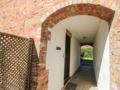 A narrow outdoor passage with a brick archway white walls a wooden door and a lattice fence at Beaver Cottage in Little Thirkleby near Thirsk