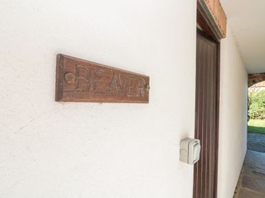 A wooden sign with the word Beaver on a white wall next to a brown door at Beaver Cottage in Little Thirkleby near Thirsk
