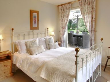 A bedroom with a double bed bedside tables lamps floral curtains and outdoor patio furniture at Beaver Cottage in Little Thirkleby near Thirsk