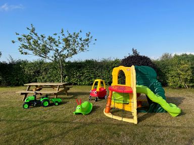 A garden with a picnic table, a toy tractor, a red toy car, a green caterpillar rocker, and a children's slide at Beaver Cottage in Little Thirkleby near Thirsk