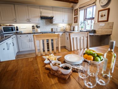 A kitchen with white cabinets wooden dining table with fruit bowl plates and wine glasses at Beaver Cottage in Little Thirkleby near Thirsk