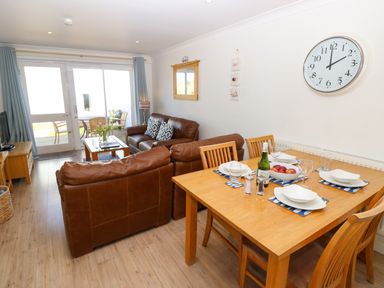 A living room with brown leather sofas a wooden dining table set for four and glass doors leading outside at Cape A9 Norton Near Freshwater