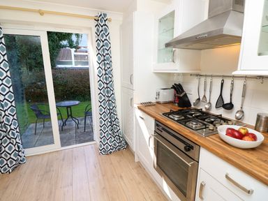 A kitchen with wooden countertop gas stove oven utensils hanging and sliding glass door leading to garden with table and chairs at Cape A9 Norton Near Freshwater