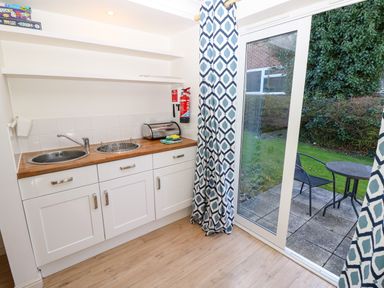A kitchenette with two sinks a bread box and a fire extinguisher next to a sliding glass door with patterned curtains leading to a patio with a table and chair at Cape A9 Norton Near Freshwater