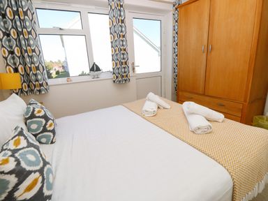 A bedroom with a bed with patterned pillows and folded towels on a yellow patterned blanket next to a wooden wardrobe at Cape A9 Norton Near Freshwater