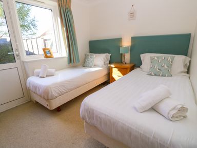 A bedroom with two single beds white linens teal cushions and a wooden nightstand with a lamp at Cape A9 Norton Near Freshwater