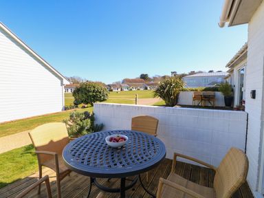 An outdoor patio with a round table and four chairs a bowl with fruit on the table and houses in the background at Cape A9 Norton Near Freshwater