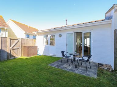A small backyard with green grass a patio area with a round table and two chairs next to a white brick house at Cape A9 Norton Near Freshwater