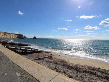 A beach with a concrete walkway and wooden groynes with cliffs in the background at Cape A9 in Norton Near Freshwater