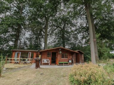 A wooden cabin with a deck and seating in the garden at Carps Well Lodge Hatton near Shrewley