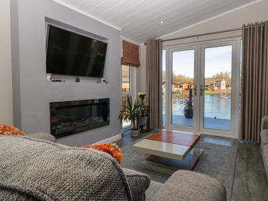 A living room with a wall-mounted tv and electric fireplace glass doors with curtains and a coffee table at Coniston View Lodge in Warton near Carnforth