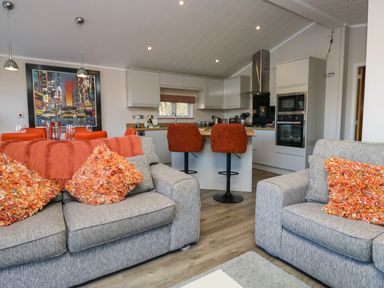 A living area with grey sofas and orange cushions facing a kitchen with bar stools at Coniston View Lodge in Warton near Carnforth