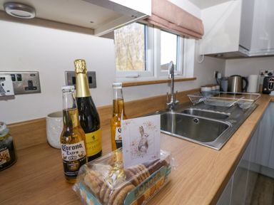 A kitchen countertop with bottles of Corona Extra and prosecco biscuits a sink and a dish rack at Coniston View Lodge in Warton near Carnforth