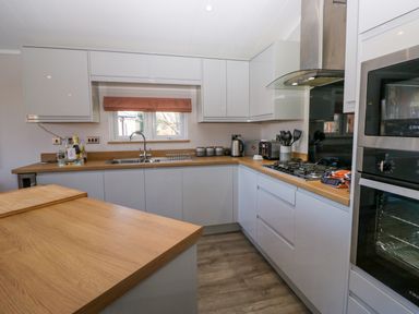 A kitchen with white cabinets wooden countertops a gas stove a sink under a window and built in ovens at Coniston View Lodge in Warton near Carnforth