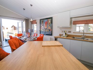 A kitchen and dining area with wooden countertops, orange chairs, a framed city painting, and open glass doors at Coniston View Lodge in Warton near Carnforth