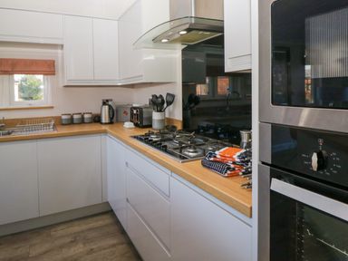 A kitchen with white cabinets a wooden countertop a gas stove a microwave oven and kitchen utensils at Coniston View Lodge in Warton near Carnforth