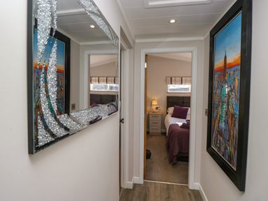 A hallway with a decorative mirror and painting leading to a bedroom with a bed and nightstand at Coniston View Lodge in Warton near Carnforth