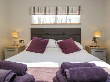 A bedroom with a double bed and purple pillows and towels at Coniston View Lodge in Warton near Carnforth