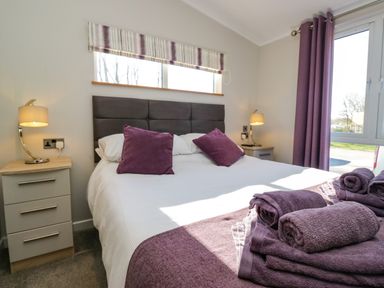 A bedroom with a double bed two purple pillows bedside tables with lamps and purple towels on the bed at Coniston View Lodge in Warton near Carnforth