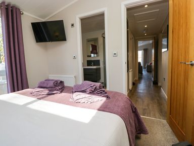 A bedroom with a bed with folded towels on it a wall mounted television a door leading to a bathroom and a hallway at Coniston View Lodge Warton near Carnforth