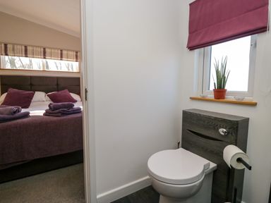 A bathroom with a toilet and a window next to a bedroom with a bed and folded towels at Coniston View Lodge in Warton near Carnforth