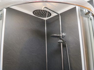 A shower enclosure with a rain showerhead and handheld shower on a dark textured wall at Coniston View Lodge in Warton near Carnforth