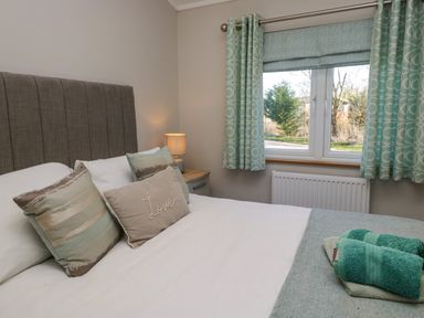 A bedroom with a bed with pillows a bedside table with a lamp a window with curtains and folded towels on the bed at Coniston View Lodge in Warton near Carnforth
