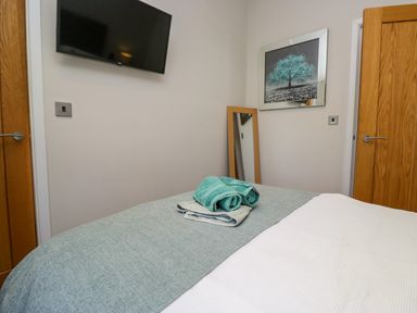A bedroom with a bed with folded towels on it a wall-mounted television two wooden doors a full-length mirror and a framed picture at Coniston View Lodge in Warton near Carnforth