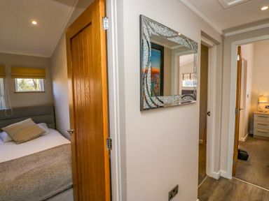 A hallway with two open wooden doors showing bedrooms and a wall mirror at Coniston View Lodge in Warton near Carnforth