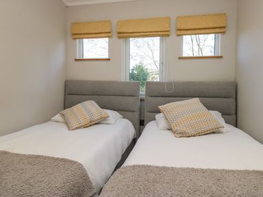 A bedroom with two single beds and three windows with blinds at Coniston View Lodge in Warton near Carnforth
