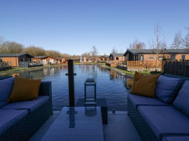 An outdoor seating area with sofas and a lantern overlooking a pond with cabins around at Coniston View Lodge in Warton near Carnforth