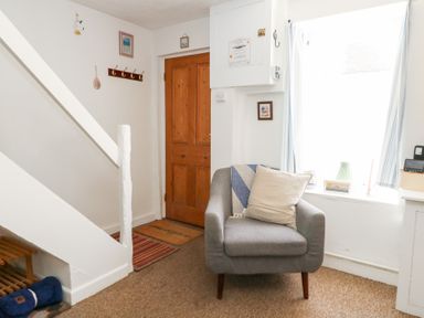 A hallway with a staircase, door, and armchair at Driftwood in Weymouth