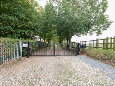 A gated entrance with trees lining the path at Pear Tree in Wood Norton