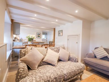 A living area with patterned sofas and cushions a wooden dining table with chairs and flowers in a vase at Harbour View in Polperro