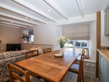 A dining area with a wooden table and four chairs with a vase of flowers on the table and a window with a blind at Harbour View in Polperro