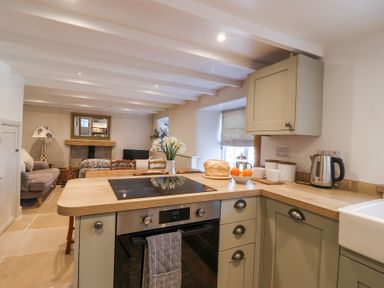 A kitchen with an oven stovetop and kettle overlooking a living area with sofas and a fireplace at Harbour View in Polperro