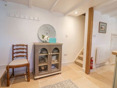A corner of a room with a wooden chair next to a cabinet holding dishes and a staircase leading upstairs at Harbour View in Polperro
