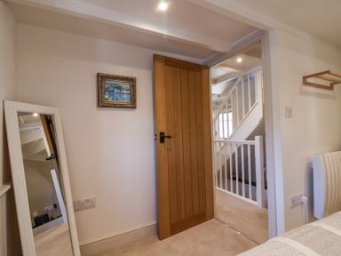 A bedroom corner with a wooden door open to a staircase and a leaning mirror on the wall at Harbour View in Polperro