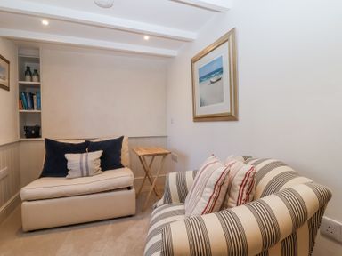 A small seating area with a striped armchair and a cream sofa with cushions and a framed beach painting on the wall at Harbour View in Polperro