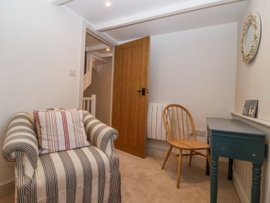 A small room with a striped armchair, wooden chair, blue desk, and a wooden door at Harbour View Polperro