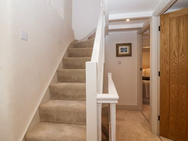 A carpeted staircase with white railing next to a hallway with wooden doors and a framed picture on the wall at Harbour View in Polperro