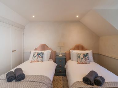 A bedroom with two single beds each with a patterned pillow and rolled towels with a bedside table and lamp at Harbour View in Polperro