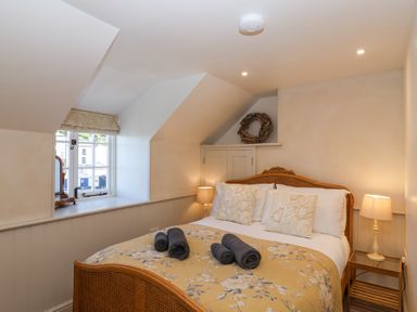 A bedroom with a wooden bed and floral bedspread two bedside tables with lamps and a window with a decorative wreath above a cupboard at Harbour View in Polperro
