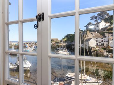A view of boats in a harbor and houses on a hill through a multi-pane window at Harbour View in Polperro