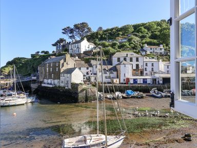 A harbor with moored boats and white buildings on a hillside viewed through an open window at Harbour View in Polperro