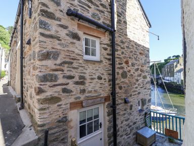 A stone building with windows and a door near a water canal with boats at Harbour View in Polperro
