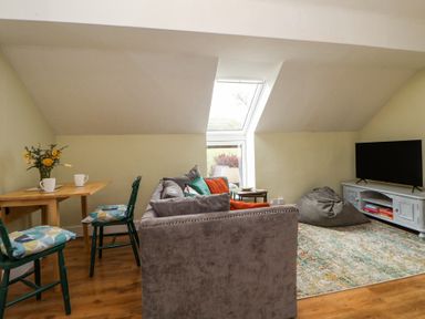 A living room with a grey sofa a wooden table with green chairs and a television on a cabinet at Cuddfan at Swallow Cottage in Rhydtalog near Coedpoeth