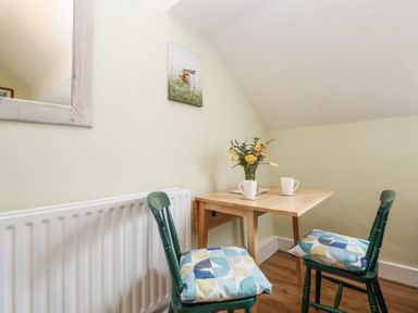 A small wooden table with two mugs and a vase of flowers with two green chairs and patterned cushions at Cuddfan at Swallow Cottage Rhydtalog near Coedpoeth