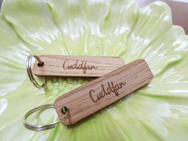 Two wooden keychains engraved with Cuddfan on a green ceramic plate shaped like a leaf at Cuddfan at Swallow Cottage in Rhydtalog near Coedpoeth