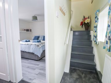 A staircase next to a bedroom with a bed and books on a shelf at Cuddfan at Swallow Cottage in Rhydtalog near Coedpoeth